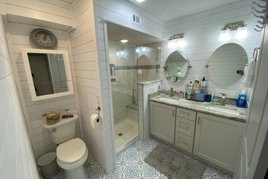 Inspiration for a mid-sized farmhouse master white tile and porcelain tile ceramic tile, multicolored floor, double-sink and shiplap wall bathroom remodel in Atlanta with flat-panel cabinets, gray cabinets, a one-piece toilet, white walls, an undermount sink, granite countertops, a hinged shower door, gray countertops and a built-in vanity