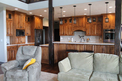 Inspiration for a large timeless l-shaped medium tone wood floor and brown floor open concept kitchen remodel in Other with raised-panel cabinets, medium tone wood cabinets, quartzite countertops, stainless steel appliances, an island, gray backsplash, stone tile backsplash and a farmhouse sink