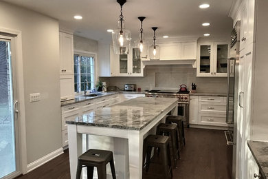 Photo of a mid-sized traditional l-shaped separate kitchen in Detroit with an undermount sink, shaker cabinets, white cabinets, marble benchtops, grey splashback, stone tile splashback, stainless steel appliances, dark hardwood floors, with island and brown floor.
