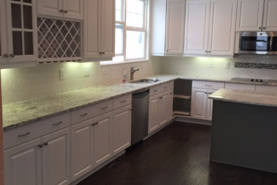 Inspiration for a large transitional l-shaped dark wood floor and brown floor eat-in kitchen remodel in Denver with a double-bowl sink, raised-panel cabinets, white cabinets, granite countertops, white backsplash, ceramic backsplash, stainless steel appliances and an island