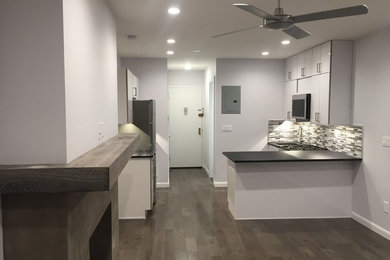 Photo of a mid-sized transitional u-shaped open plan kitchen in New York with an undermount sink, flat-panel cabinets, white cabinets, solid surface benchtops, multi-coloured splashback, matchstick tile splashback, stainless steel appliances, dark hardwood floors, a peninsula, brown floor, black benchtop and vaulted.