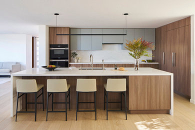 Inspiration for a large modern galley medium tone wood floor and brown floor open concept kitchen remodel in Los Angeles with a double-bowl sink, flat-panel cabinets, medium tone wood cabinets, quartz countertops, white backsplash, quartz backsplash, stainless steel appliances, an island and white countertops