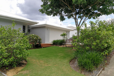 Small tropical front yard full sun garden in Sunshine Coast with a garden path and decking for summer.