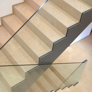 Photo of a large contemporary curved glass railing staircase in Other with limestone treads and limestone risers.