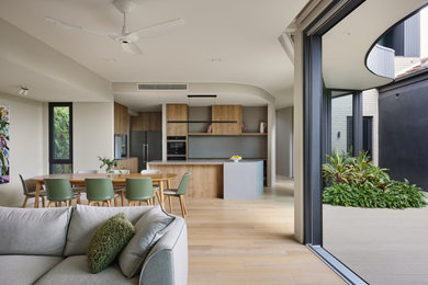 Mid-sized contemporary open plan kitchen in Melbourne with flat-panel cabinets, light wood cabinets, concrete benchtops, grey splashback, engineered quartz splashback, black appliances, medium hardwood floors, with island and grey benchtop.