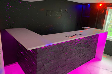 Example of a mid-sized minimalist look-out marble floor basement design in Other with a bar, black walls and a stone fireplace