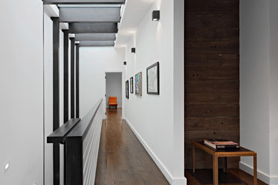 This is an example of a mid-sized modern hallway in New York with white walls, dark hardwood floors, wood walls and brown floor.