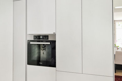 Inspiration for a medium sized contemporary grey and cream l-shaped enclosed kitchen in Other with an integrated sink, flat-panel cabinets, white cabinets, glass worktops, grey splashback, glass sheet splashback, integrated appliances, ceramic flooring, a breakfast bar, grey floors, grey worktops and feature lighting.