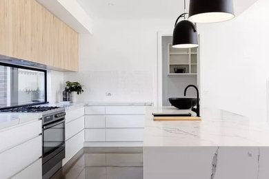 Photo of a mid-sized contemporary l-shaped eat-in kitchen in Melbourne with flat-panel cabinets, light wood cabinets, quartz benchtops, white splashback, black appliances, concrete floors, with island and white benchtop.
