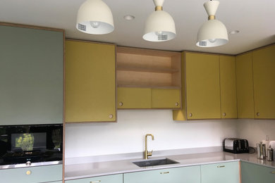 This is an example of a medium sized retro l-shaped kitchen/diner in London with a submerged sink, flat-panel cabinets, composite countertops, white splashback, glass sheet splashback, integrated appliances, porcelain flooring, an island, grey floors and grey worktops.