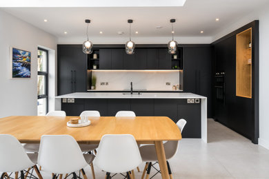 Modern kitchen in Other with a single-bowl sink, flat-panel cabinets, black cabinets, quartz worktops, white splashback, integrated appliances, concrete flooring, an island, grey floors and white worktops.