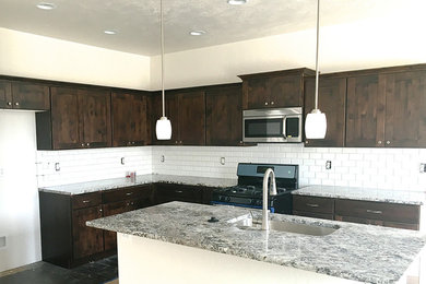 Cottage l-shaped kitchen photo in Boise with an undermount sink, shaker cabinets, dark wood cabinets, granite countertops, white backsplash, subway tile backsplash, stainless steel appliances and an island