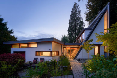 This is an example of a large midcentury two-storey stucco white house exterior in Vancouver with a shingle roof.