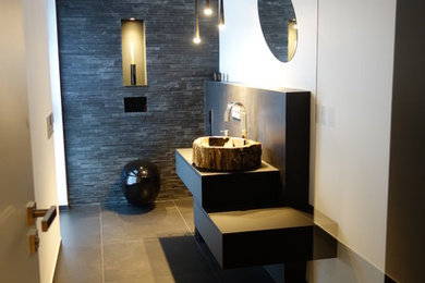 Mittelgroße Moderne Gästetoilette mit flächenbündigen Schrankfronten, schwarzen Schränken, Wandtoilette, schwarzen Fliesen, weißer Wandfarbe, Wandwaschbecken, Waschtisch aus Holz und schwarzem Boden in Stuttgart