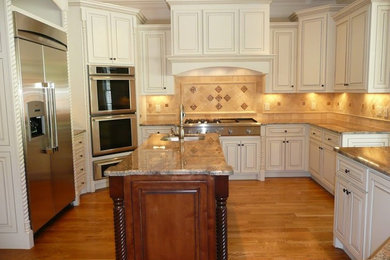 Example of a mid-sized u-shaped medium tone wood floor open concept kitchen design in Nashville with an undermount sink, white cabinets, granite countertops, beige backsplash, stainless steel appliances, an island, raised-panel cabinets and stone tile backsplash