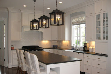 Mid-sized elegant l-shaped dark wood floor and brown floor kitchen photo in Other with a farmhouse sink, shaker cabinets, white cabinets, quartzite countertops, white backsplash, subway tile backsplash and an island