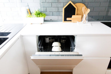 Diseño de cocina contemporánea con fregadero de doble seno, encimera de acrílico, salpicadero verde, electrodomésticos negros, suelo de madera clara y suelo beige