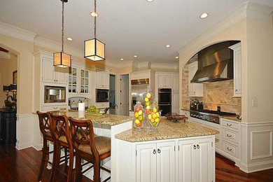 Example of a large classic l-shaped medium tone wood floor eat-in kitchen design in Indianapolis with an undermount sink, raised-panel cabinets, white cabinets, granite countertops, beige backsplash, stone tile backsplash, stainless steel appliances and an island