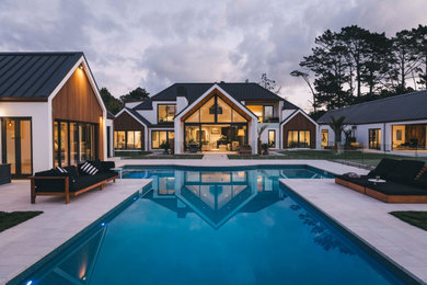 Large trendy white two-story adobe exterior home photo in Auckland with a metal roof and a black roof
