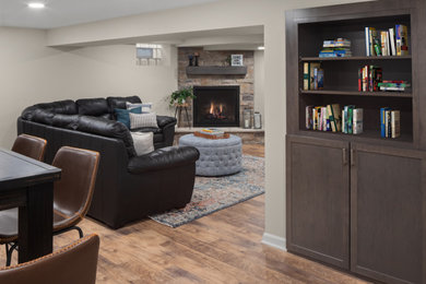 This is an example of a medium sized fully buried basement in Milwaukee with beige walls, vinyl flooring, a standard fireplace, a stone fireplace surround and brown floors.