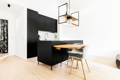 Offene, Kleine Moderne Küche mit Unterbauwaschbecken, schwarzen Schränken, Edelstahl-Arbeitsplatte, schwarzen Elektrogeräten, hellem Holzboden, Kücheninsel, braunem Boden und grauer Arbeitsplatte in München