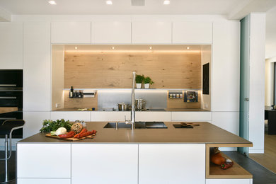 Geschlossene, Zweizeilige, Mittelgroße Moderne grifflose Küche mit integriertem Waschbecken, flächenbündigen Schrankfronten, weißen Schränken, Küchenrückwand in Braun, Rückwand aus Holz, schwarzen Elektrogeräten, zwei Kücheninseln, grauem Boden und grauer Arbeitsplatte in Frankfurt am Main