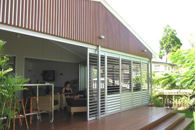 Design ideas for a mid-sized beach style backyard screened-in verandah in Brisbane with decking and a roof extension.