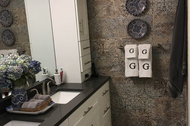 This is an example of a mid-sized mediterranean 3/4 bathroom in Miami with shaker cabinets, white cabinets, an alcove shower, multi-coloured tile, cement tile, multi-coloured walls, medium hardwood floors, an undermount sink, solid surface benchtops, grey floor, a hinged shower door and black benchtops.
