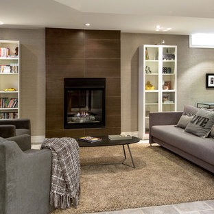 Modelo de sótano con ventanas actual con paredes grises, chimenea tradicional, marco de chimenea de baldosas y/o azulejos y suelo de baldosas de cerámica