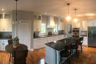 Example of a laminate floor and brown floor kitchen design in Other with a single-bowl sink, shaker cabinets, white cabinets, quartzite countertops, white backsplash, subway tile backsplash, stainless steel appliances, an island and gray countertops