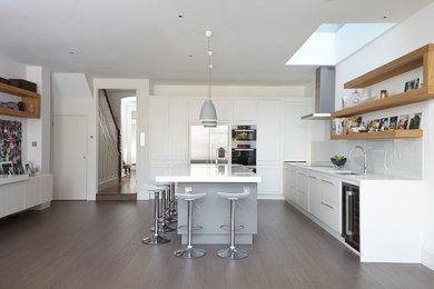 Design ideas for a contemporary l-shaped kitchen in London with a submerged sink, flat-panel cabinets, white cabinets, white splashback, glass sheet splashback, stainless steel appliances, medium hardwood flooring and an island.