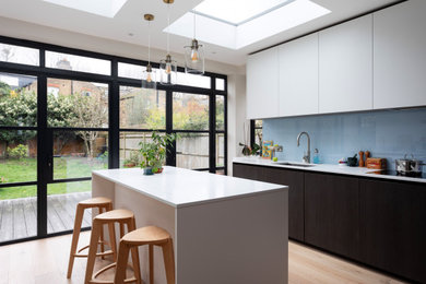 Inspiration for a large victorian grey and white u-shaped kitchen/diner in London with a submerged sink, flat-panel cabinets, dark wood cabinets, composite countertops, blue splashback, glass sheet splashback, integrated appliances, light hardwood flooring, an island, beige floors, white worktops and feature lighting.