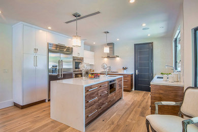 Example of a large transitional u-shaped medium tone wood floor and brown floor eat-in kitchen design in Los Angeles with an undermount sink, flat-panel cabinets, white cabinets, quartz countertops, white backsplash, porcelain backsplash, stainless steel appliances, an island and white countertops