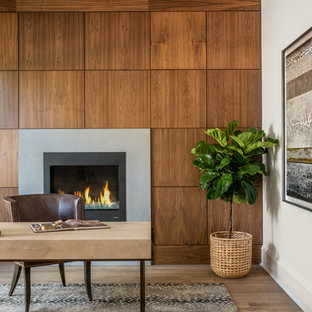 This is an example of a transitional home office in Charlotte with white walls, medium hardwood floors, a standard fireplace, a concrete fireplace surround and a freestanding desk.