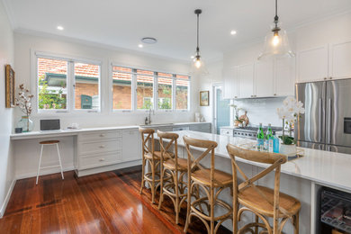 Large transitional l-shaped open plan kitchen in Brisbane with a double-bowl sink, shaker cabinets, grey cabinets, solid surface benchtops, white splashback, subway tile splashback, stainless steel appliances, dark hardwood floors, with island and white benchtop.