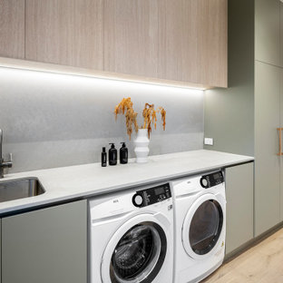 Foto di una lavanderia multiuso contemporanea di medie dimensioni con lavello sottopiano, ante verdi, top in marmo, paraspruzzi grigio, paraspruzzi in lastra di pietra, pareti bianche, parquet chiaro e lavatrice e asciugatrice affiancate