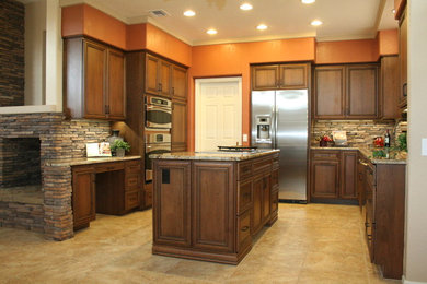 This is an example of a mid-sized traditional u-shaped eat-in kitchen in Phoenix with an undermount sink, raised-panel cabinets, dark wood cabinets, granite benchtops, brown splashback, stone tile splashback, stainless steel appliances, linoleum floors and with island.