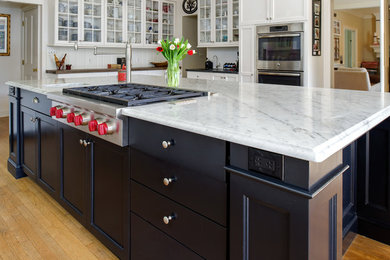 This is an example of a large traditional u-shaped eat-in kitchen in DC Metro with an undermount sink, shaker cabinets, white cabinets, soapstone benchtops, white splashback, window splashback, stainless steel appliances, medium hardwood floors, with island, brown floor and black benchtop.