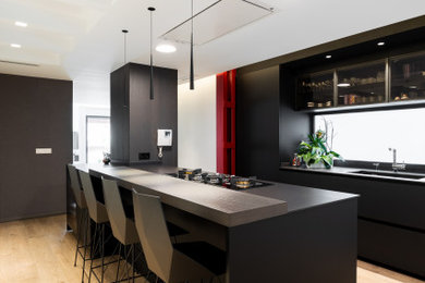 Inspiration for a large contemporary galley open plan kitchen in Valencia with black appliances, medium hardwood floors, with island, black benchtop, flat-panel cabinets, black cabinets, mirror splashback and beige floor.