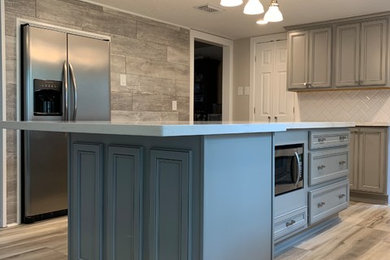 Example of a classic single-wall bamboo floor and beige floor kitchen pantry design in Houston with recessed-panel cabinets, gray cabinets, solid surface countertops, white backsplash, an island, beige countertops, subway tile backsplash, stainless steel appliances and a farmhouse sink