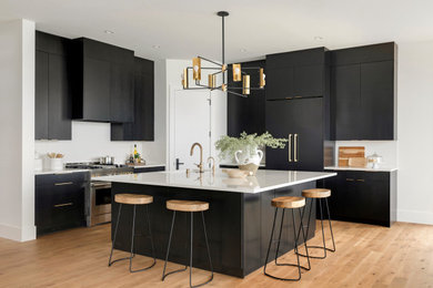 Photo of a contemporary l-shaped open plan kitchen in Minneapolis with an undermount sink, flat-panel cabinets, black cabinets, panelled appliances, medium hardwood floors, with island, brown floor and white benchtop.