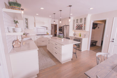 Example of a large transitional u-shaped light wood floor and brown floor eat-in kitchen design in Portland with a farmhouse sink, shaker cabinets, white cabinets, solid surface countertops, white backsplash, subway tile backsplash, stainless steel appliances and an island