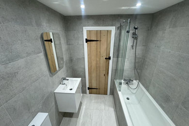 Small contemporary grey and white bathroom in Surrey with shaker cabinets, white cabinets, an alcove bath, an alcove shower, a one-piece toilet, grey tiles, grey walls, ceramic flooring, a wall-mounted sink, granite worktops, grey floors, a sliding door, white worktops, a single sink, a floating vanity unit, a coffered ceiling and ceramic tiles.