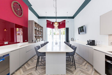 Photo of an expansive kitchen in Surrey with a double-bowl sink, flat-panel cabinets, grey cabinets, glass tile splashback, laminate floors and with island.