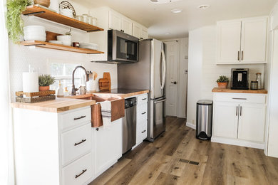 Example of a small farmhouse galley laminate floor and gray floor kitchen design in Portland with a farmhouse sink, raised-panel cabinets, white cabinets, wood countertops, white backsplash, porcelain backsplash, stainless steel appliances and no island