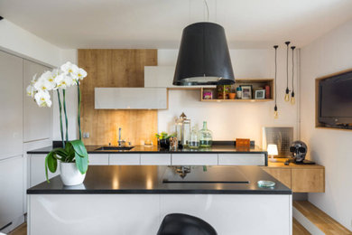 Cette image montre une cuisine ouverte linéaire design de taille moyenne avec un évier 1 bac, un placard à porte plane, des portes de placard beiges, un plan de travail en granite, une crédence blanche, une crédence en bois, un électroménager noir, parquet clair, îlot, un sol beige et plan de travail noir.