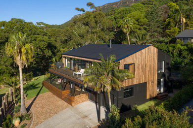 Photo of a mid-sized beach style two-storey house exterior in Wollongong with wood siding, a gable roof, a tile roof and a black roof.