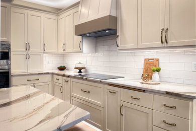 Inspiration for a large classic l-shaped kitchen in Milwaukee with a submerged sink, recessed-panel cabinets, white cabinets, engineered stone countertops, white splashback, ceramic splashback, stainless steel appliances, laminate floors, an island, brown floors and white worktops.