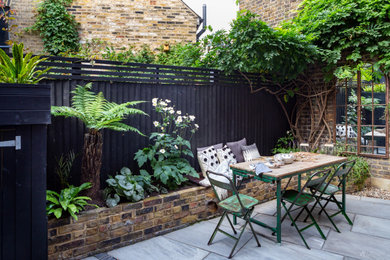 Design ideas for a small victorian back partial sun garden for summer in London with a raised bed, natural stone paving and a wood fence.