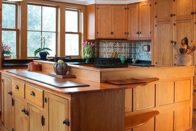 Eat-in kitchen - mid-sized craftsman u-shaped medium tone wood floor eat-in kitchen idea in Other with an undermount sink, recessed-panel cabinets, medium tone wood cabinets, soapstone countertops, metallic backsplash, metal backsplash, black appliances and an island